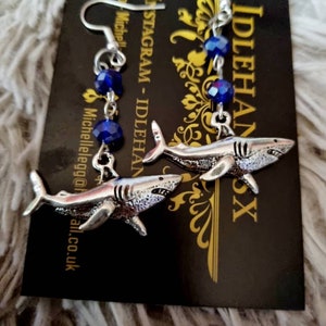 Pode incluir: Brincos de tubar&atilde;o prateados com contas de cristal azul. Os brincos est&atilde;o pendurados em um cart&atilde;o preto com o texto "INSTAGRAM - IDLEHANDSX" nele.