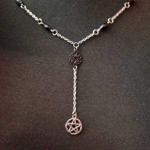 May include: A silver chain necklace with black beads and a silver pendant featuring a pentagram. The pendant hangs from a silver chain with a black filigree charm.