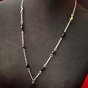 May include: A silver chain necklace with black beads and a small black pendant. The necklace has two gold crescent moon charms.
