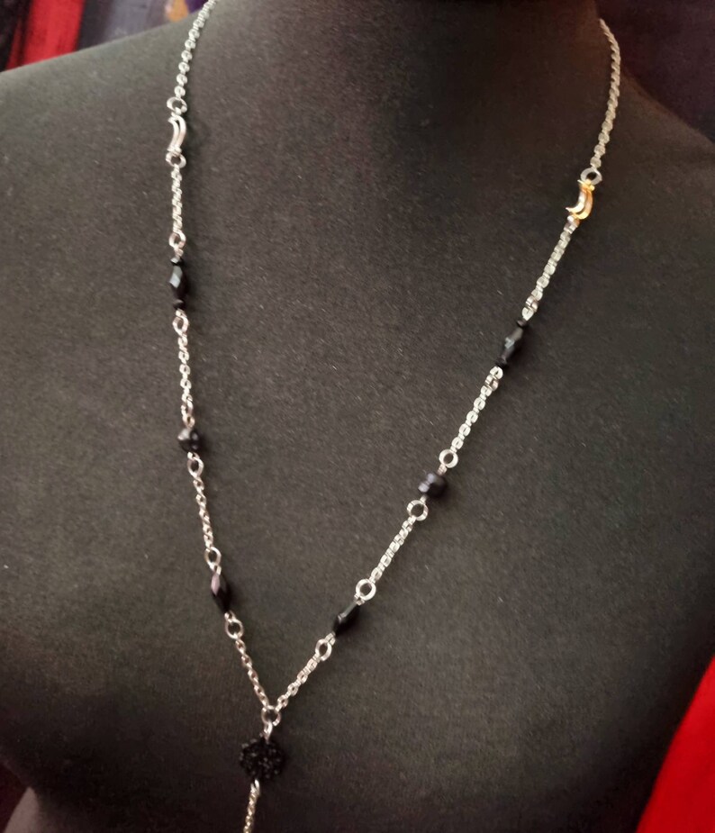 May include: A silver chain necklace with black beads and a small black pendant. The necklace has two gold crescent moon charms.