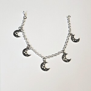 May include: A silver chain bracelet with five delicate crescent moon charms. The moons have a filigree design and are connected to the chain with small loops.