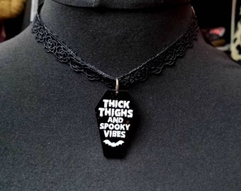 May include: Black choker necklace with a black coffin-shaped pendant that says "Thick Thighs and Spooky Vibes" in white text with a white bat graphic.
