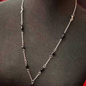 May include: A silver chain necklace with black beads and a black metal pendant. The necklace has a gold clasp.