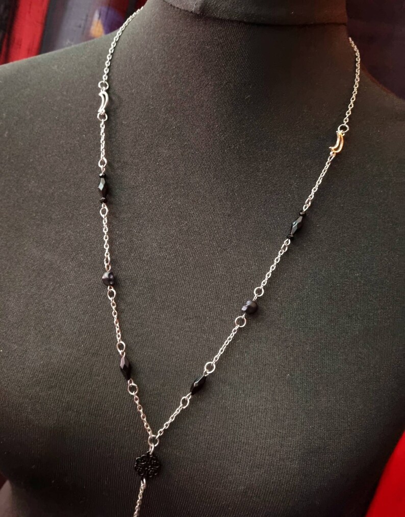 May include: A silver chain necklace with black beads and a black metal pendant. The necklace has a gold clasp.