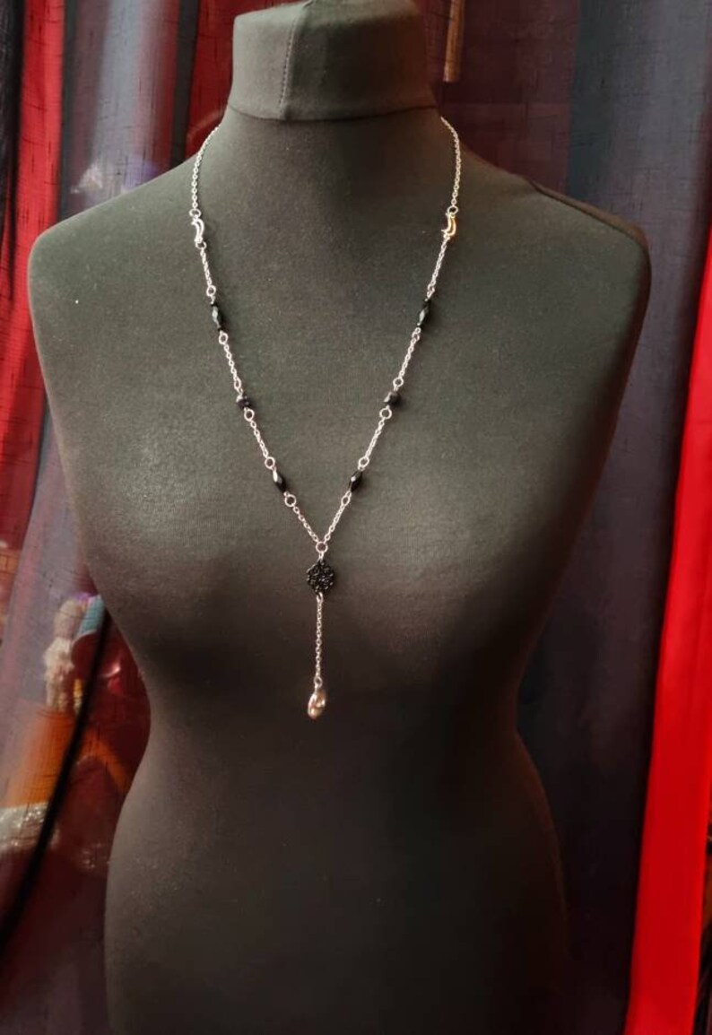 May include: A silver chain necklace with black beads and a silver pendant. The pendant is a small, intricate design with a skull at the bottom.