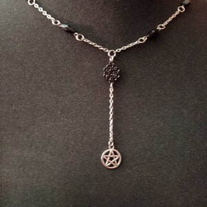 May include: A silver chain necklace with black beads and two silver charms. The charms are a circle with a pentagram and a circle with a floral design.