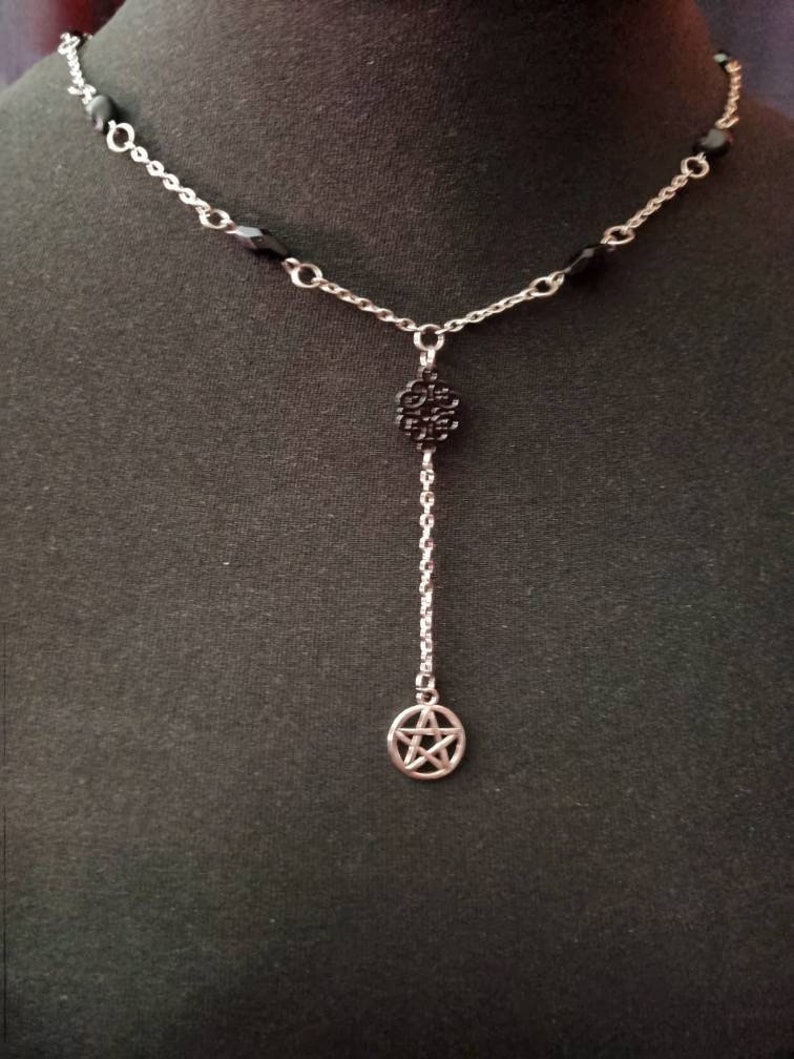 May include: A silver chain necklace with black beads and two silver charms. The charms are a circle with a pentagram and a circle with a floral design.