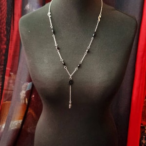May include: A silver chain necklace with black beads and a black pendant. The pendant is a small, intricate design.