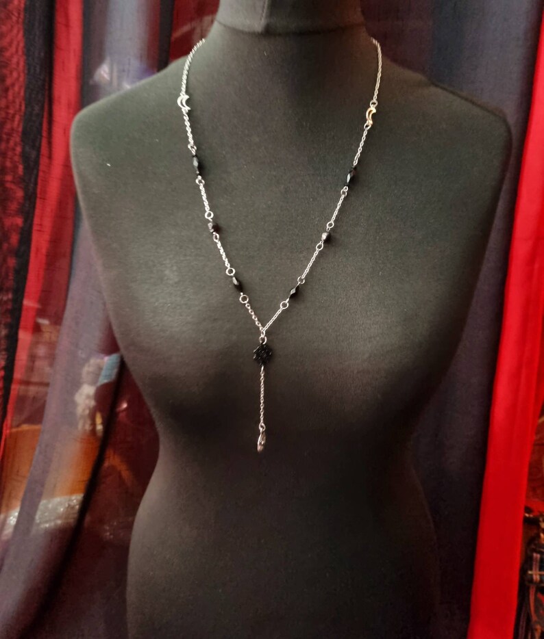 May include: A silver chain necklace with black beads and a black pendant. The pendant is a small, intricate design.