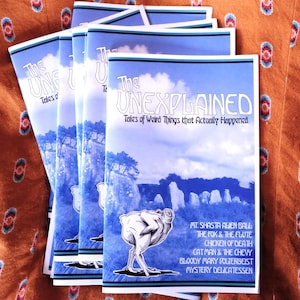 May include: A stack of booklets titled "The UNEXPLAINED: Tales of Weird Things that Actually Happened." Each booklet features a blue cover with a landscape illustration and a drawing of a chicken-like creature. The titles of the stories are listed below the illustration.
