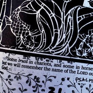 K&ouml;nnte beinhalten: Schwarz-Wei&szlig;-Kunstdruck mit stilisierten Fisch- und Blumenmustern. Das Bild enth&auml;lt Text aus Psalm 20,7 mit den Worten "Die einen verlassen sich auf Wagen und die andern auf Rosse; wir aber gedenken des Namens des HERRN, unseres Gottes."