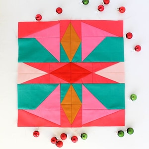 May include: A colorful quilt block with a geometric design featuring pink, red, teal, and gold fabric. The block is surrounded by small red and green ornaments.