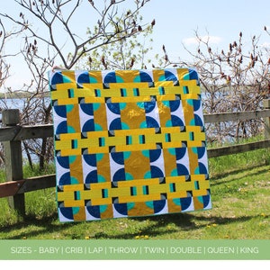 May include: A quilt pattern called "Lunar Eclipse" with a modern design featuring yellow, blue, and white circles and rectangles. The quilt is displayed outdoors against a backdrop of trees and a lake. The pattern is available in sizes: baby, crib, lap, throw, twin, double, queen, and king.
