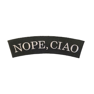 以下が含まれることがあります： 黒い刺繍パッチに白い文字で「NOPE, CIAO」と書いてあります。