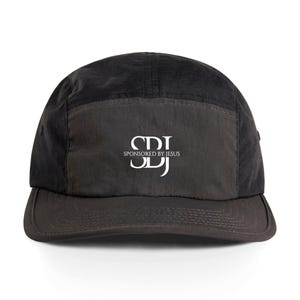 Op de afbeelding: Zwarte vijf-panel cap met een gebogen klep. De cap heeft een rechthoekig vlak aan de voorkant met de witte tekst "SDJ SPONSORED BY JESUS". De cap is gemaakt van een mat, licht glanzend materiaal.