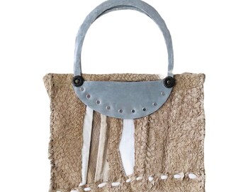 Può includere: Una piccola borsa a mano di colore marrone chiaro, con una texture ruvida, con manico in metallo argentato e dettagli decorativi in metallo. La borsa ha un aspetto unico e fatto a mano.