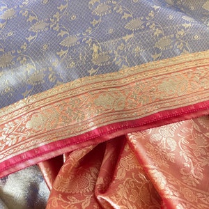 Może przedstawiać: Sari z jedwabiu w kolorze niebieskim i złotym z wzorem i czerwoną i złotą lam&oacute;wką. Sari jest złożone na p&oacute;ł, a lam&oacute;wka jest widoczna.