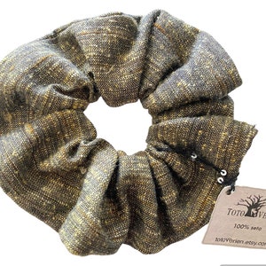 May include: A brown and gold scrunchie made from 100% silk. The scrunchie has a textured fabric and is tied with a black string. The scrunchie has a small tag attached to it that says "Toto Verien 100% seta totoverien.etsy.com".