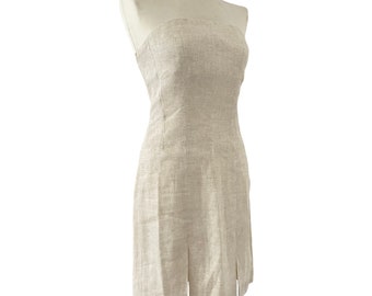 May include: A beige strapless dress made of textured fabric. The knee-length dress has a front slit. The dress is displayed on a mannequin. The dress is a neutral colour.
