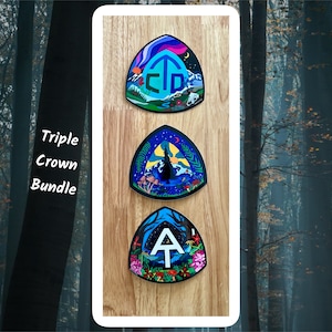 Puede incluir: Paquete Triple Crown de tres señales de sendero de senderismo ilustradas. Las señales son triangulares y presentan una combinación de colores azul, negro y verde. Las señales están montadas sobre un fondo de madera.