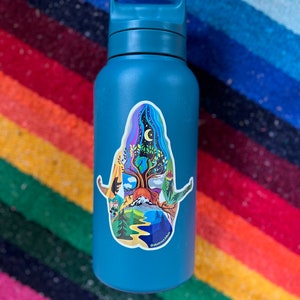Puede incluir: Una botella de agua azul verdosa con una pegatina colorida de un &aacute;rbol con una luna y estrellas en el fondo. La pegatina tiene el texto "@abbyfrancesart" en la parte inferior.