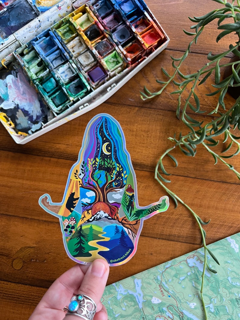 May include: A holographic sticker featuring a colorful illustration of a person meditating with a tree growing from their head. The tree is surrounded by nature scenes, including mountains, a river, and a moon. The sticker has the text "@abstract.hikes" at the bottom.