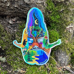 May include: A holographic sticker featuring a colorful illustration of a person meditating with a tree growing from their chest. The tree has a crescent moon in the sky above it and a variety of nature elements surrounding it, including mountains, a river, and a bird. The sticker has the text "@abstract.hikes" at the bottom.