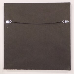 May include: The back of a framed picture with a dark brown frame and a black hanging wire with two metal hooks.