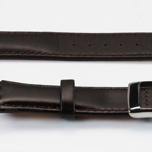 K&ouml;nnte beinhalten: Ein braunes Lederarmband mit einer silbernen Schlie&szlig;e. Das Armband hat einen gen&auml;hten Rand und ist f&uuml;r eine Uhr mit einer Bandansto&szlig;breite von 18 mm ausgelegt.