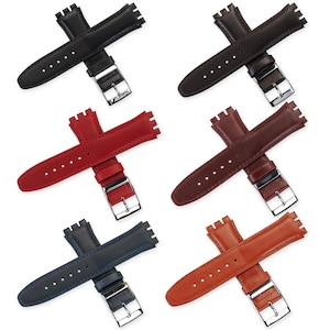 Könnte beinhalten: Sechs Leder-Armbänder in verschiedenen Farben: Schwarz, Dunkelbraun, Rot, Mittelbraun, Marineblau und Orangebraun. Jedes Armband hat eine silberfarbene Schnalle und ein markantes, gezahntes Ende zur Befestigung.