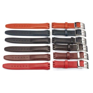 K&ouml;nnte beinhalten: Acht verschiedene farbige Lederarmb&auml;nder mit silbernen Schlie&szlig;en. Die Armb&auml;nder sind in Reihen angeordnet, wobei die oberste Reihe orange, die zweite Reihe dunkelblau, die dritte Reihe schwarz, die vierte Reihe braun, die f&uuml;nfte Reihe burgunderrot und die unterste Reihe rot ist.