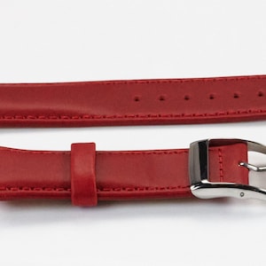K&ouml;nnte beinhalten: Rotes Lederarmband mit silberner Schlie&szlig;e. Das Armband hat eine strukturierte Oberfl&auml;che und ist mit wei&szlig;em Garn vern&auml;ht.