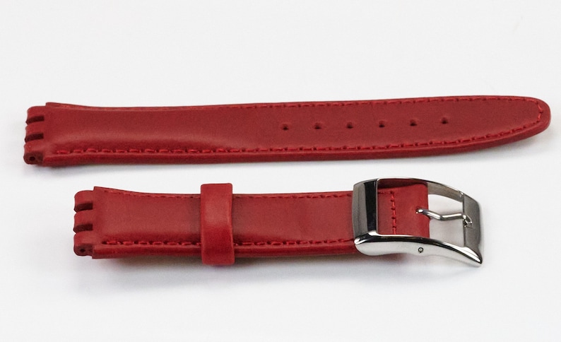 K&ouml;nnte beinhalten: Rotes Lederarmband mit silberner Schlie&szlig;e. Das Armband hat eine strukturierte Oberfl&auml;che und ist mit wei&szlig;em Garn vern&auml;ht.