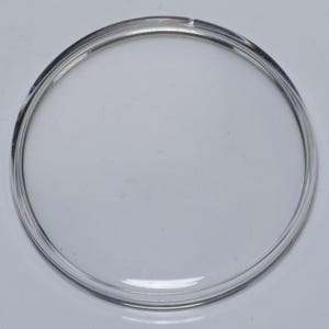 May include: A clear, circular glass object with a raised, rounded edge. The transparent material allows light to pass through, creating a subtle play of reflections. The object's design is simple and functional, suitable for various uses.