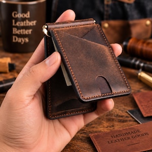 Puede incluir: Una cartera de cuero marrón oscuro con clip para billetes, acabado desgastado, costuras en contraste visibles y varias ranuras para tarjetas. La cartera incluye un clip metálico en la parte superior y una muesca para el pulgar al frente.