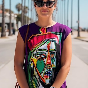 May include: A purple sleeveless dress featuring a vibrant, multi-colored abstract face graphic on the front. The design includes bold geometric shapes in red, blue, green, and yellow, with a grid pattern at the hem and a round neckline.