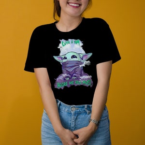 May include: Black t-shirt featuring a cartoon character with large ears, a purple cloak, and the text "CUTE I AM" and "ADORE ME YOU MUST" in green and white. The character is set against a white and purple background.