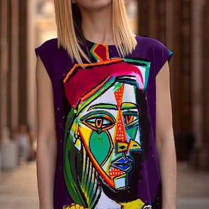 May include: A sleeveless purple tunic dress featuring a large, colorful, abstract cubist-style portrait graphic on the front. The design incorporates vibrant shades of green, yellow, red, and blue in a geometric pattern with bold black outlines.