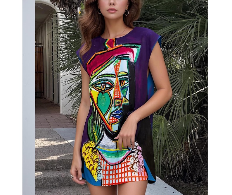 May include: A sleeveless mini dress featuring a vibrant, abstract cubist-style portrait print. The design incorporates bold blocks of purple, yellow, green, red, and blue, with a prominent face graphic centered on the front of the garment.
