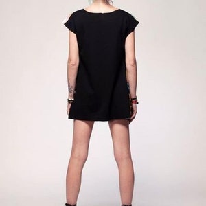 May include: A short-sleeved black dress with a solid black back and a colorful patterned front panel. The garment features a simple round neckline and a straight hemline that falls above the knees, paired with black ankle boots.