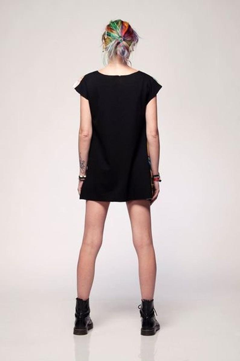 May include: A short-sleeved black dress with a solid black back and a colorful patterned front panel. The garment features a simple round neckline and a straight hemline that falls above the knees, paired with black ankle boots.