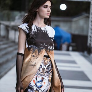 Peut inclure: Une femme portant un haut &agrave; imprim&eacute; abstrait noir et blanc avec une jupe &agrave; imprim&eacute; hibou marron et blanc. La jupe a une fente &agrave; l'avant et le haut est superpos&eacute; &agrave; la jupe.