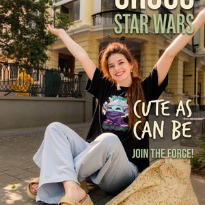 May include: A person wearing a black Grogu Star Wars t-shirt with the text "Cute as can be" and "Join the Force!". The person is wearing light blue pants and tan sandals. A floral patterned bag is next to them.