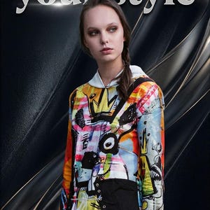 Może przedstawiać: Kobieta w kolorowej bluzie z kapturem z napisem "Change your style". Bluza ma żywy, abstrakcyjny wz&oacute;r i czarny panel. Tło to ciemny, teksturowany wz&oacute;r.