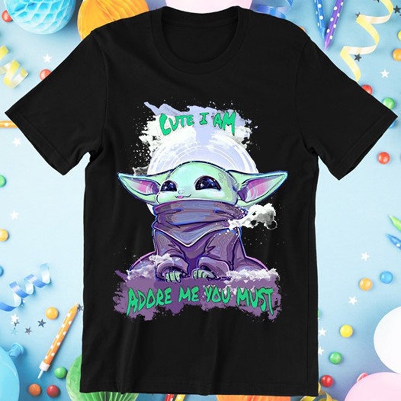 May include: Black t-shirt featuring a cartoon character with large ears, a purple cloak, and the text "Cute I Am" and "Adore Me You Must". The character is set against a white background resembling a moon.