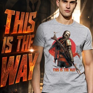 Op de afbeelding: Grijs t-shirt met een afbeelding van een personage met helm en wapen, tegen een rode cirkel. De tekst "THIS IS THE WAY" staat op het shirt en op de achtergrond.