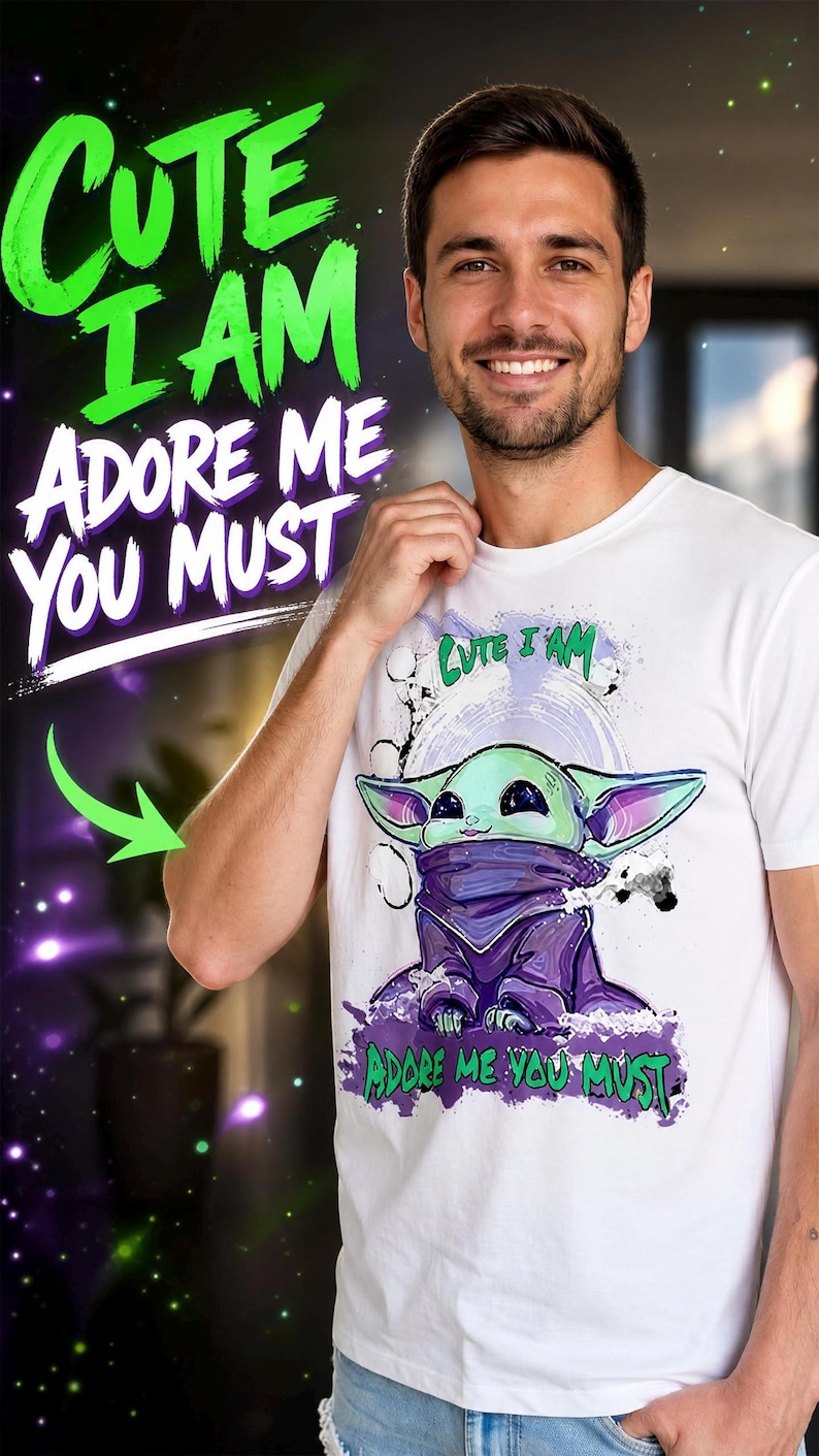 May include: White t-shirt featuring a cartoon character with the text "Cute I Am, Adore Me You Must" in green and purple. The graphic depicts a green and purple alien-like creature. The shirt is worn by a person.