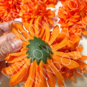 Op de afbeelding: Close-up van feloranje kunstbloemen met groene centra. De stoffen bloemblaadjes zijn in een cirkelvorm gerangschikt. De bloemen zijn waarschijnlijk voor decoratieve doeleinden.