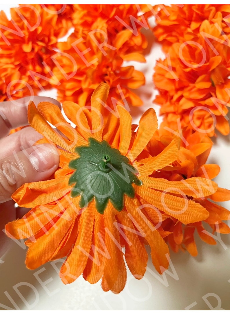 Op de afbeelding: Close-up van feloranje kunstbloemen met groene centra. De stoffen bloemblaadjes zijn in een cirkelvorm gerangschikt. De bloemen zijn waarschijnlijk voor decoratieve doeleinden.