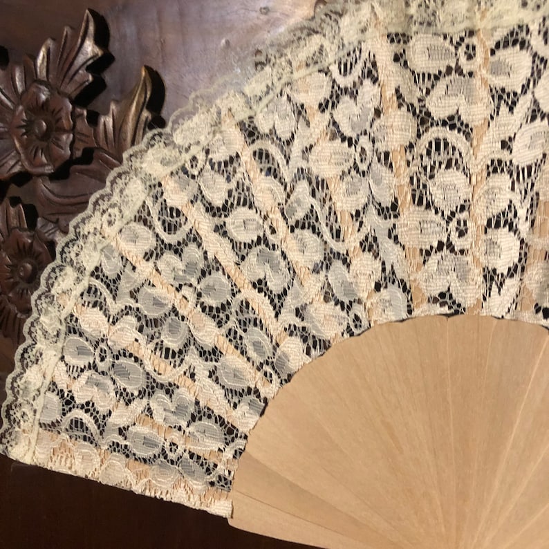 May include: A white lace fan with a wooden handle. The lace has a delicate floral pattern.
